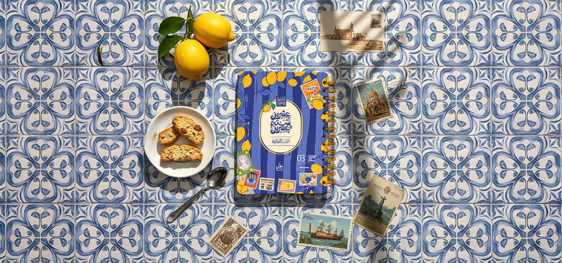 Packaged food on a blue and white patterned tablecloth with lemons and small postcards.slider_item_r4ygqT